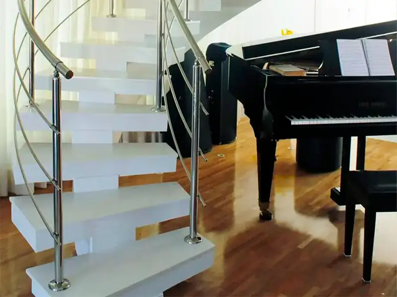 A imagem mostra uma escada branca com corrimão de aço inoxidável e um piano de cauda em uma sala de estar